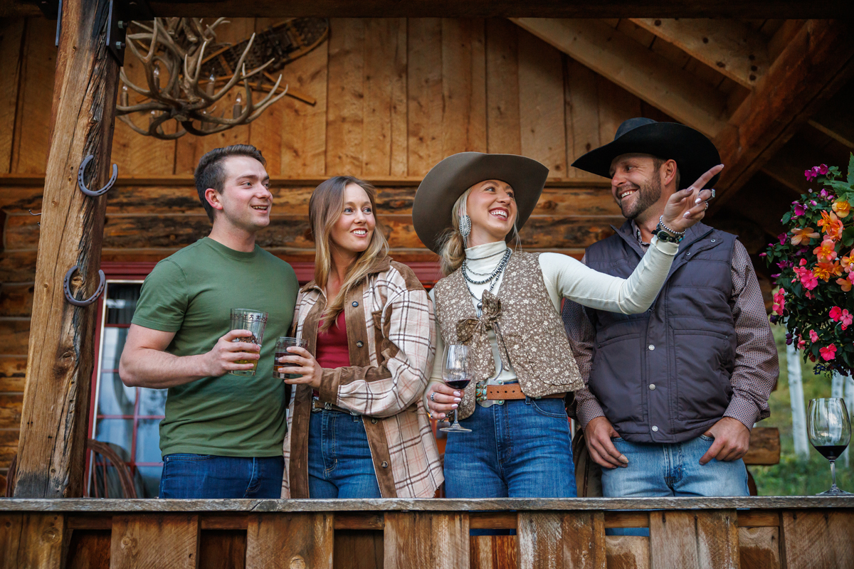 A group gathered on a porch overlooking The Home Ranch in Colorado while adventuring in the great outdoors.