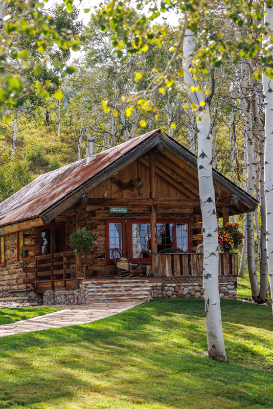 This modern wood cabin at The Home Ranch in Colorado has a cozy outdoor deck and welcoming stone walkway.