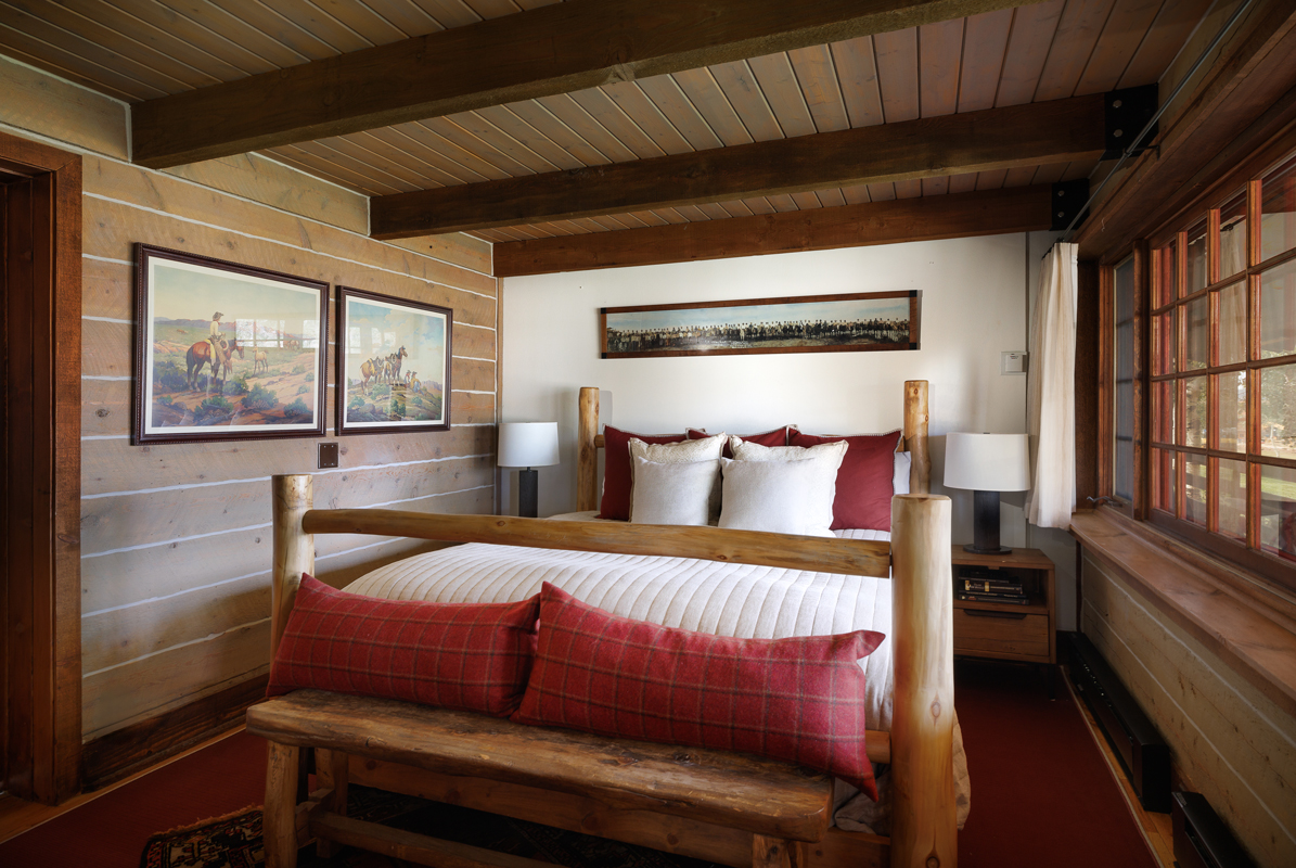 The cozy king-size bedroom of the Kanga guest cabin includes warm fabrics, wood walls, and king-sized bed.