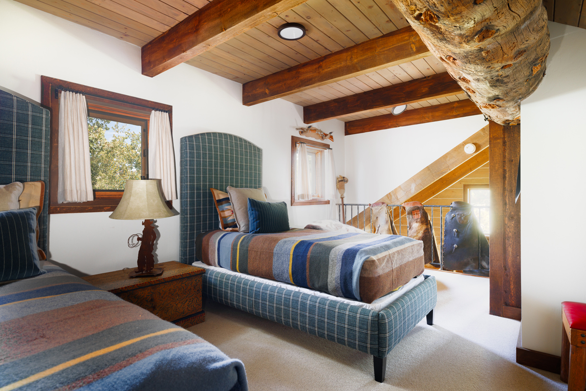 The sleeping loft in the Kanga guest cabin is decked out with leather chaps, warm fabrics, natural wood logs, and two twin beds.