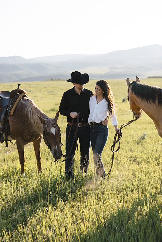 Young couple in field with horses at The Home Ranch in Colorado.